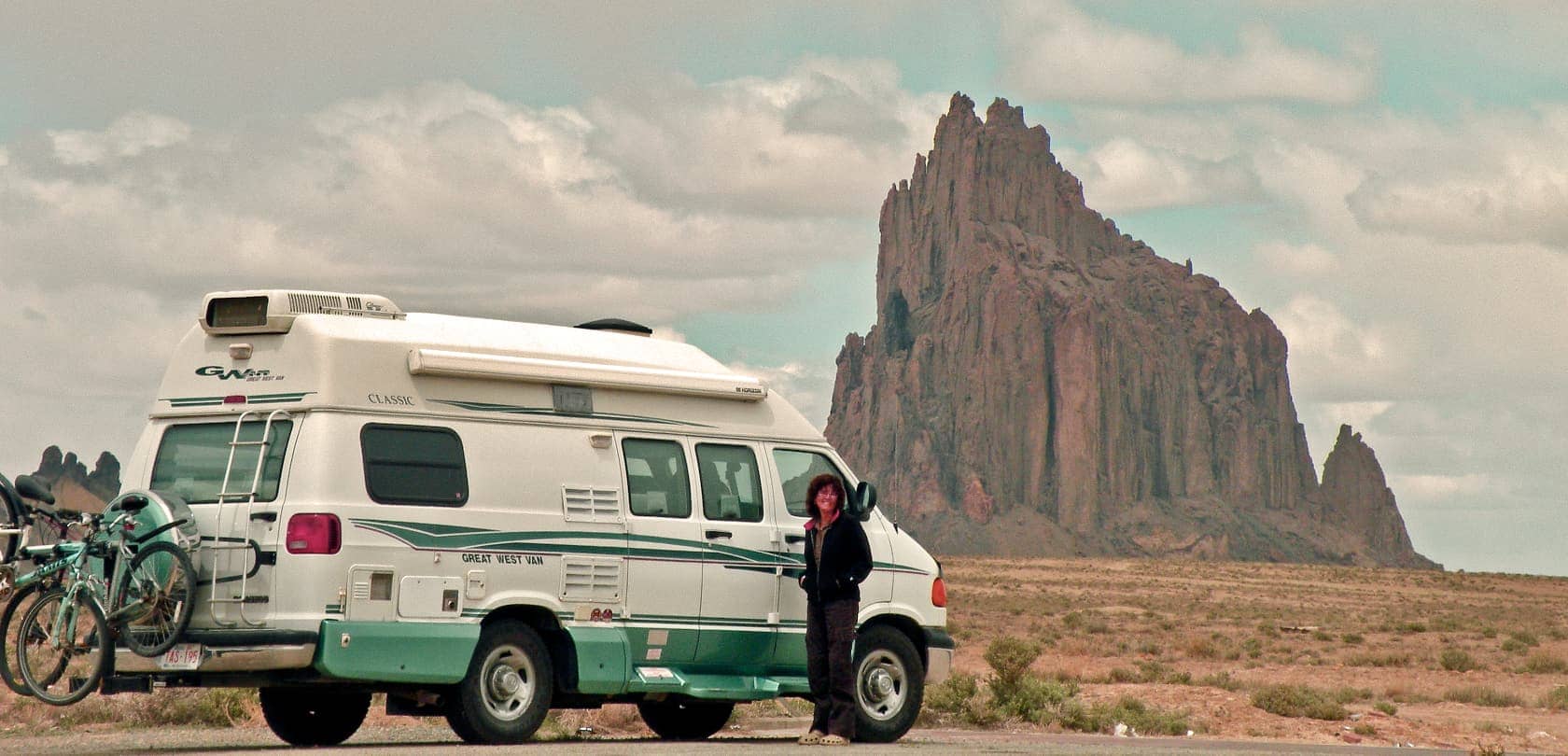 Woman standing next to van with large natural rock structure in background