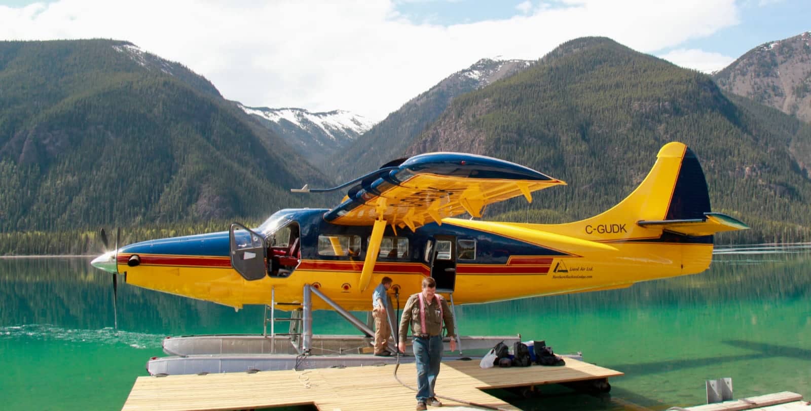 Yellow float plane on turquoise lake with mountains in background