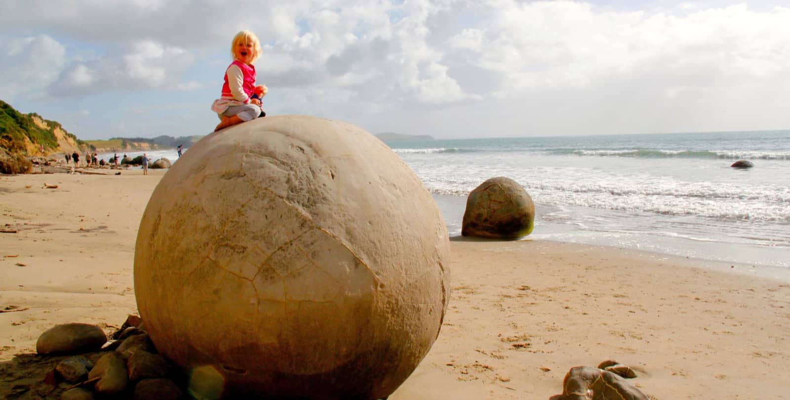 Blonde haired child sitting on large boulder on beach in New Zealand