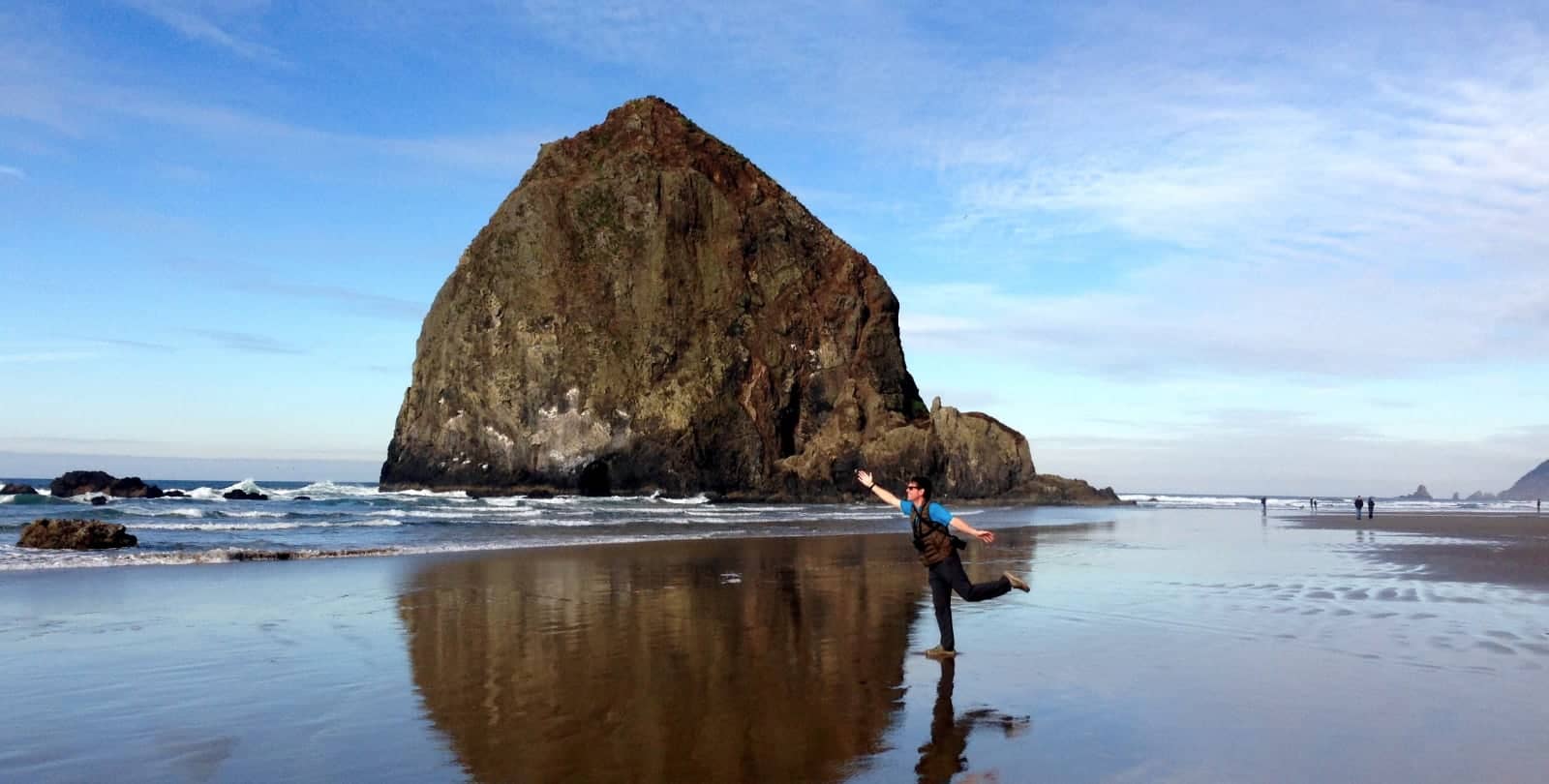 Man posing in front of big rock on beach in Oregon