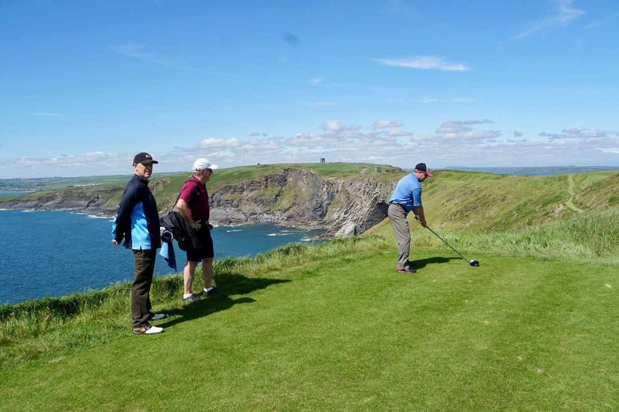 Golfer teeing off on course along coast