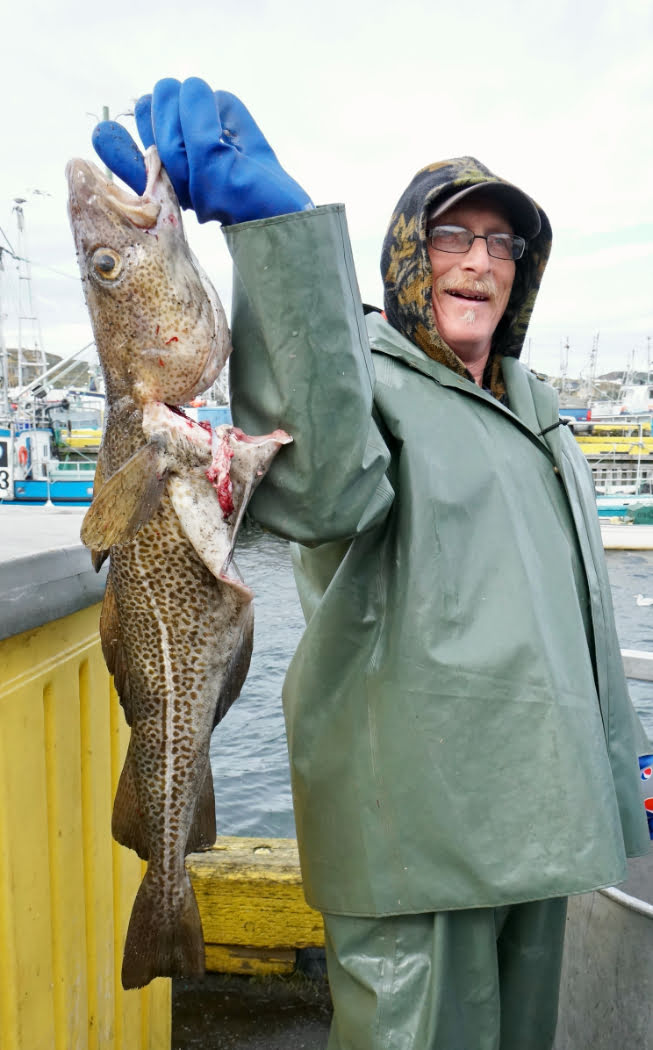 A man in a rain jacket wearing blue gloves holds up a fish and smiles
