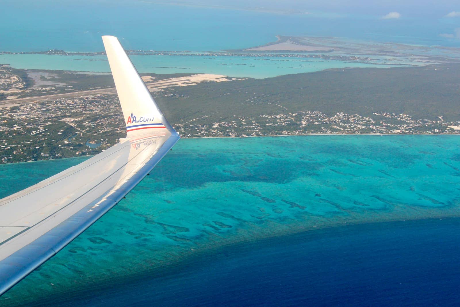 Airplane wing tip in foreground with tropical island and ocean in background