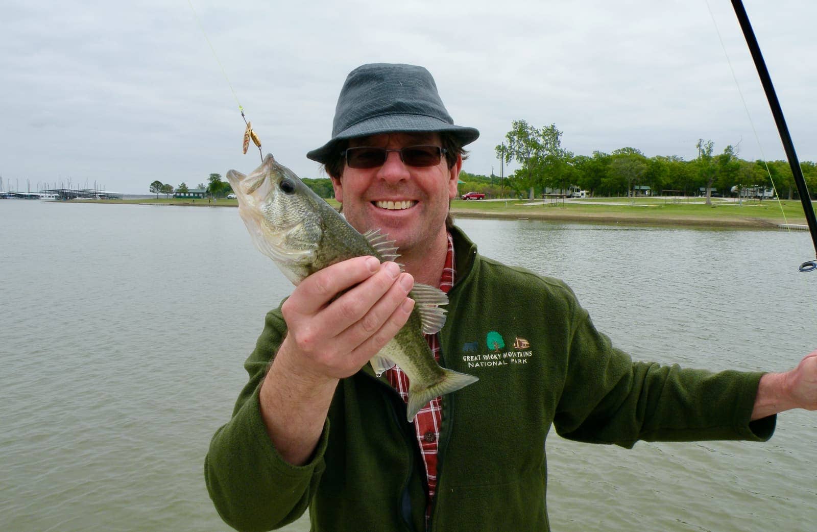 Man with hat and green jacket holding small fish