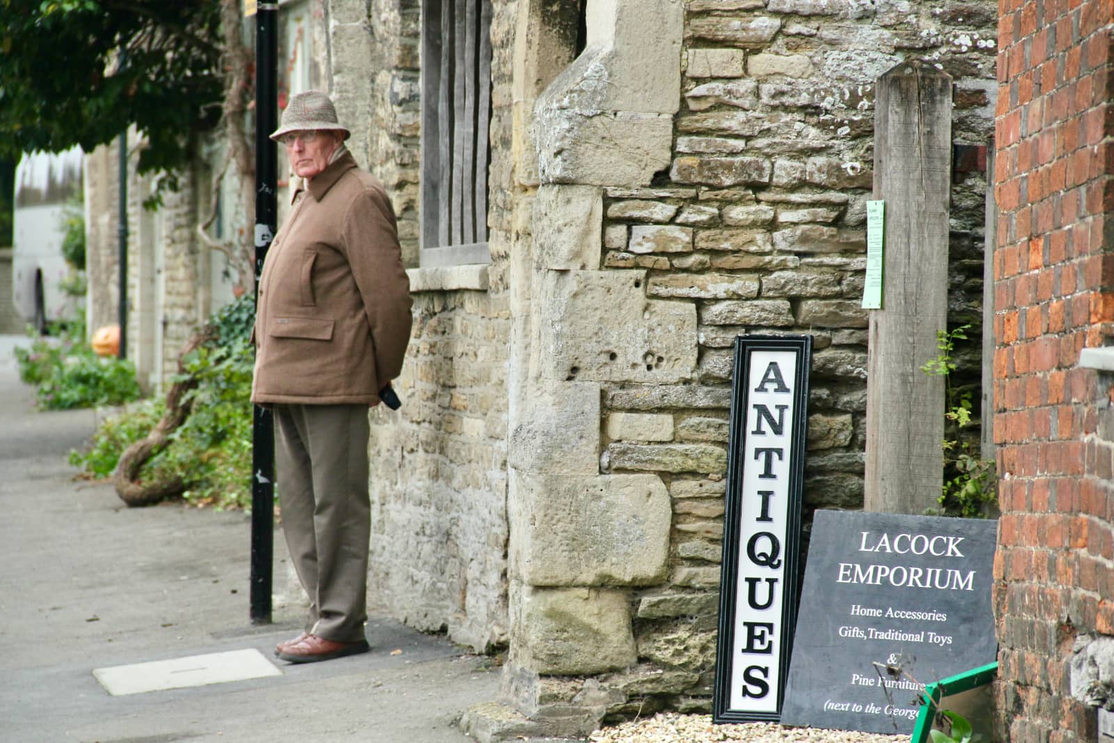 Elderly man standing against wall with antiques sign in foreground