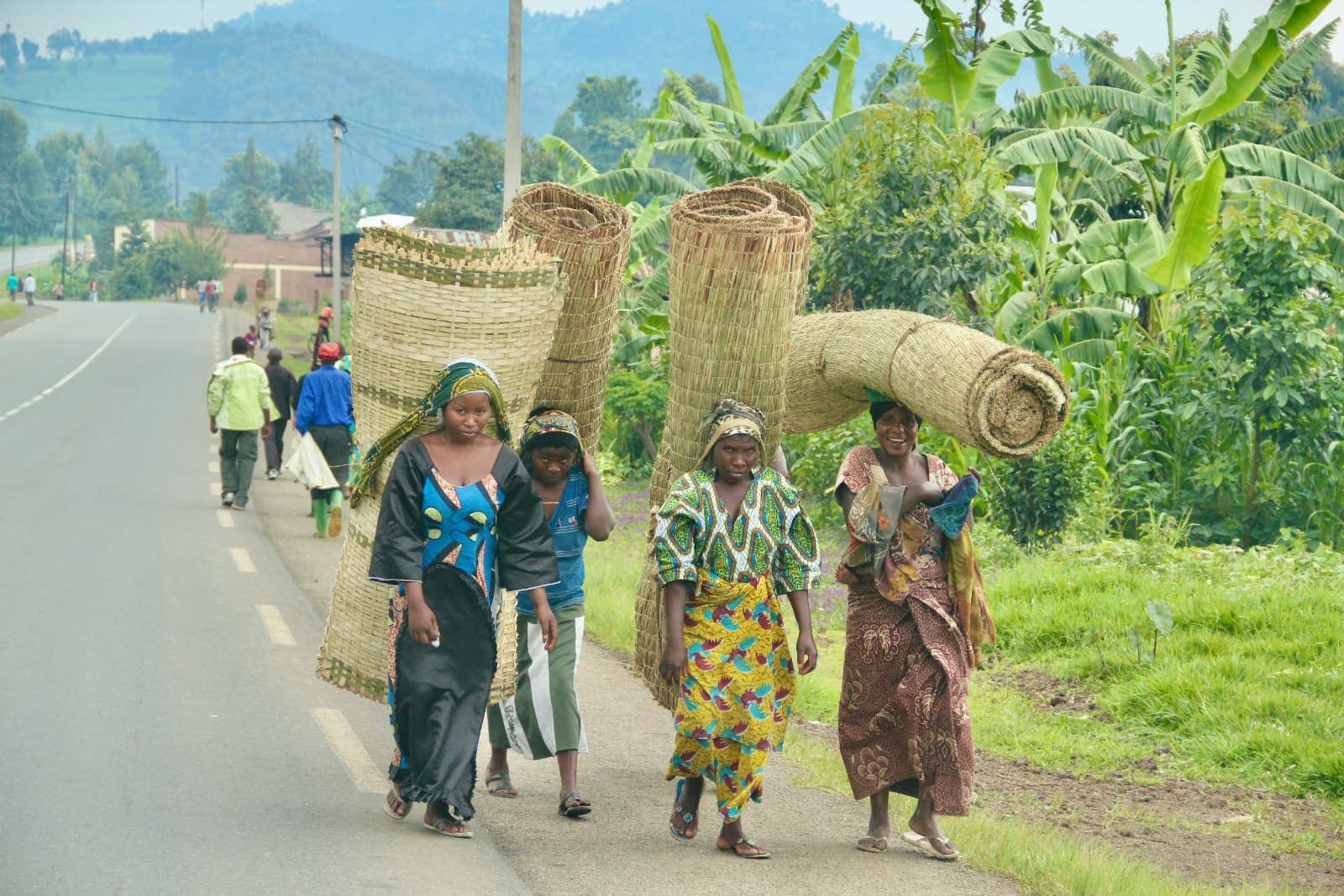 Four African women walking on roadway carrying hand woven textiles