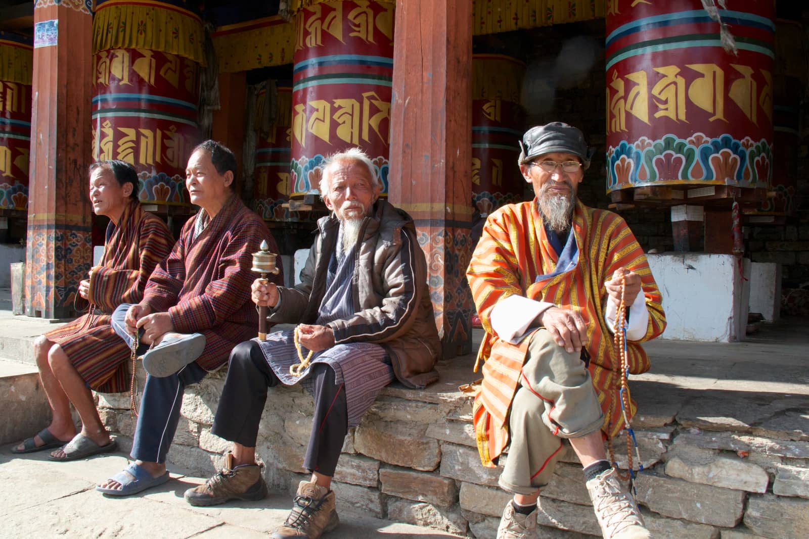 Four elderly men sitting in front of large prayer wheels