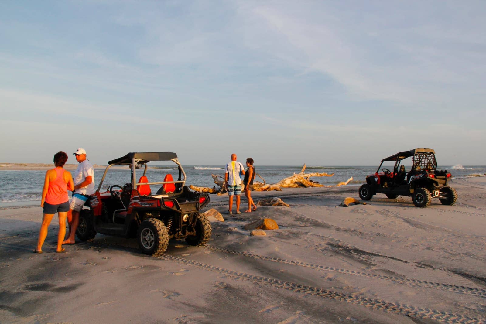 Four people standing on beach with all terrain vehicles