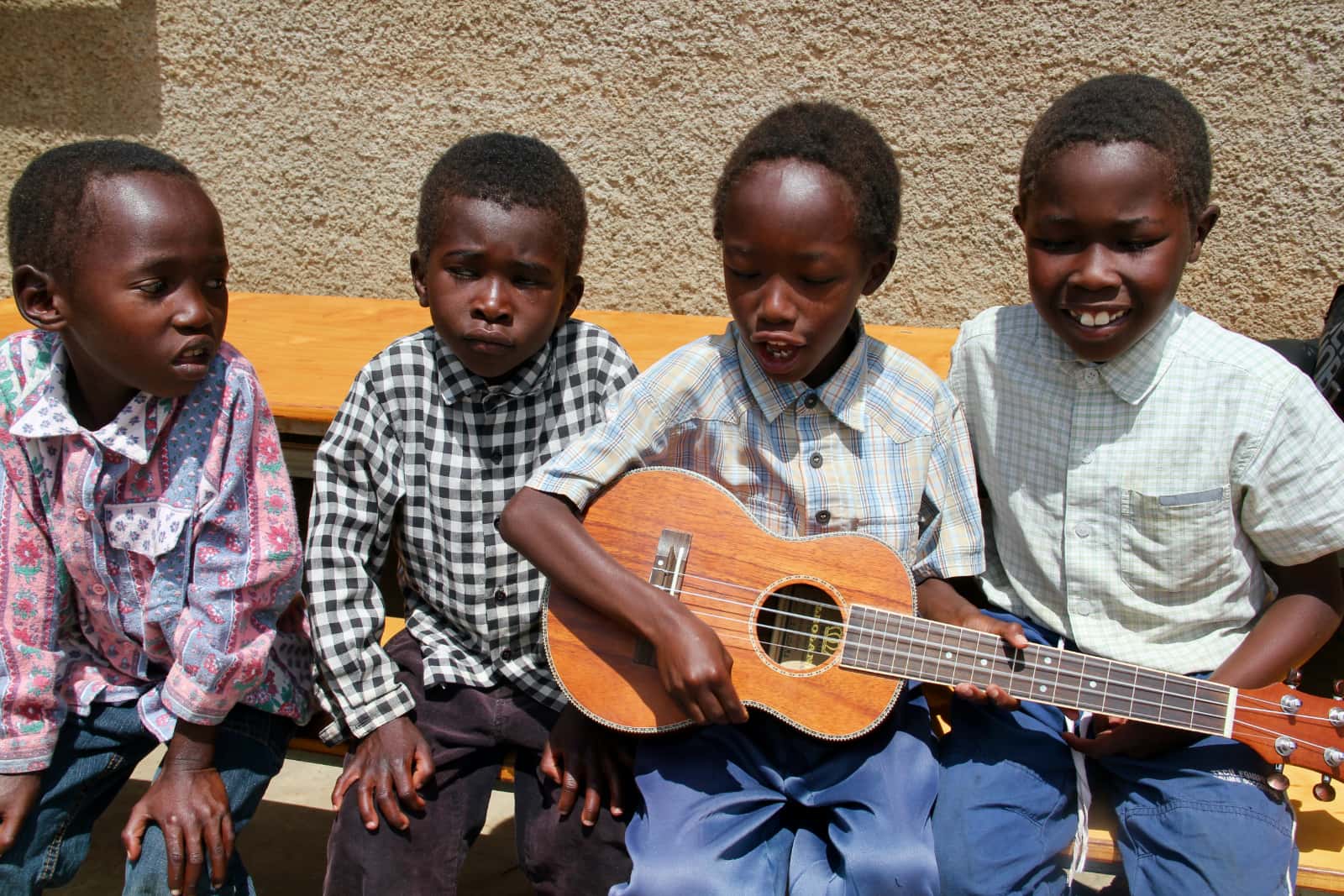 Four young African children sitting on bench with ukulele