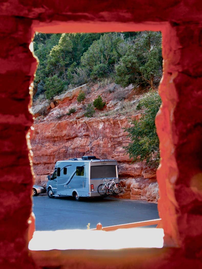 Grey RV viewed through square opening in rock