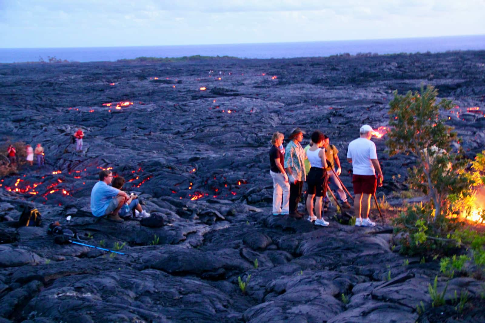 Group of people admiring flowing lava at sunset