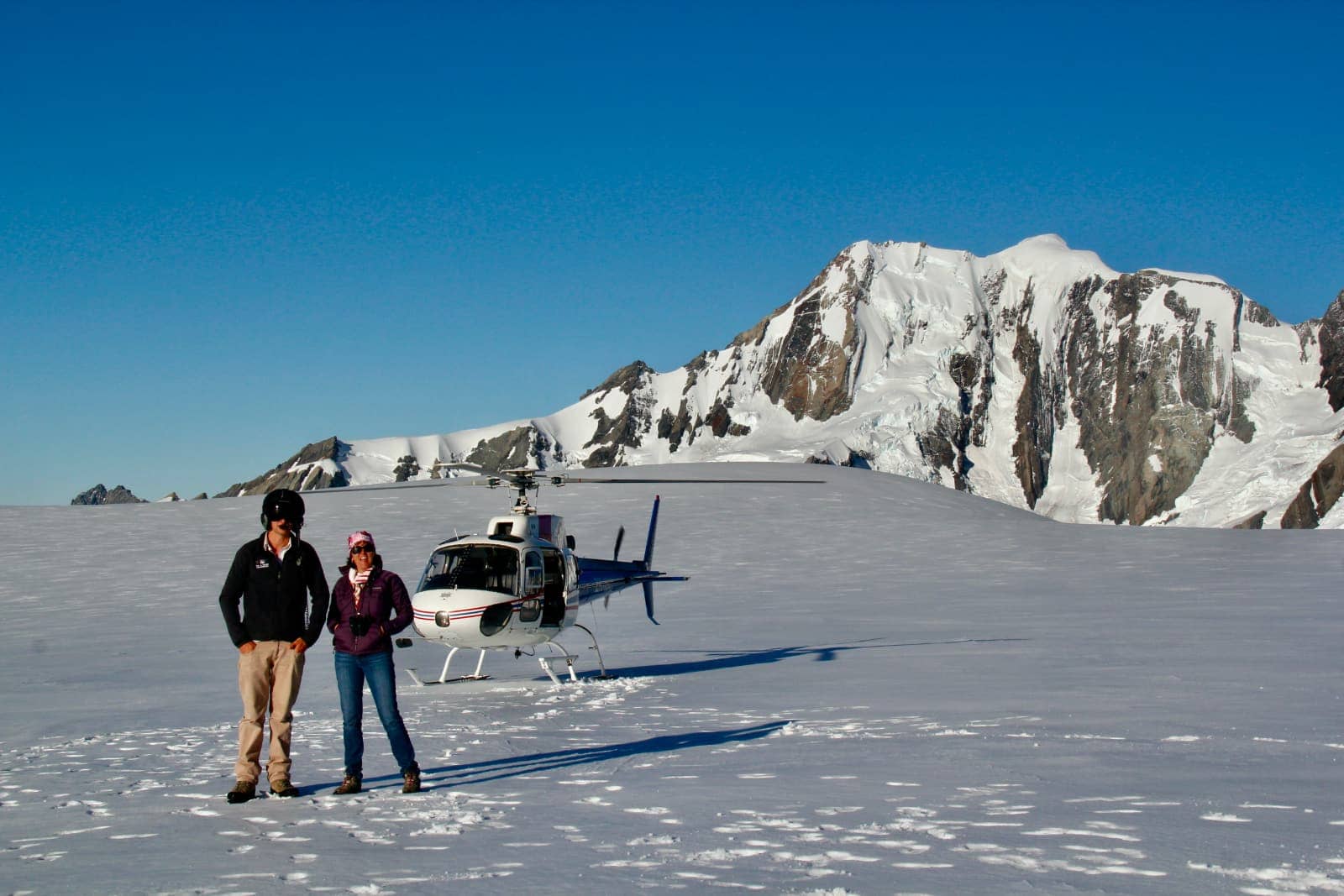 Man and woman posing on glacier with helicopter in background