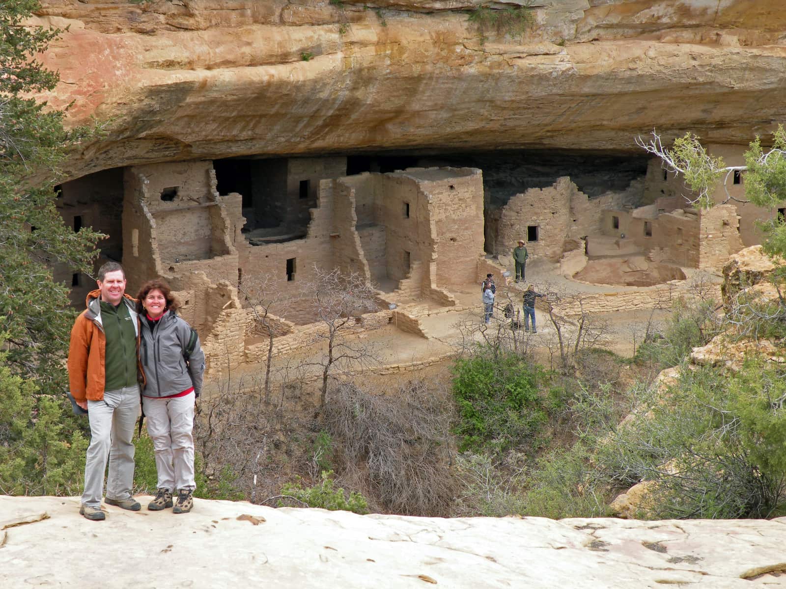 Man and woman standing in foreground with indigenous dwelling in background