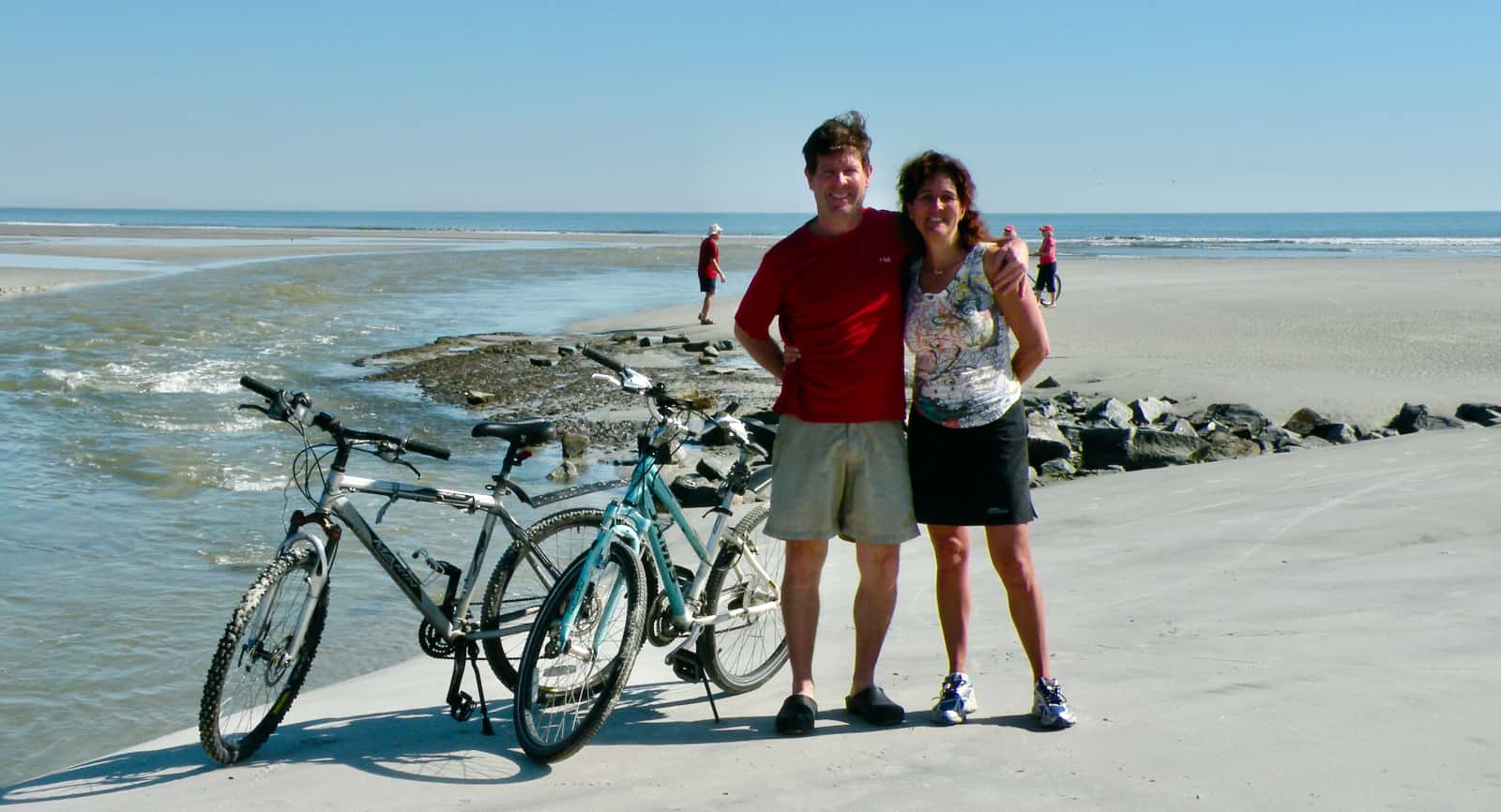 Man and woman standing with bikes with ocean in background