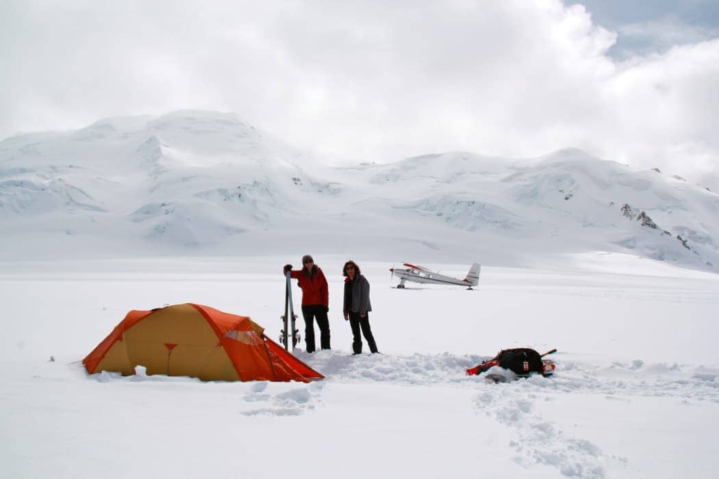 Man and woman standing with skis and tent