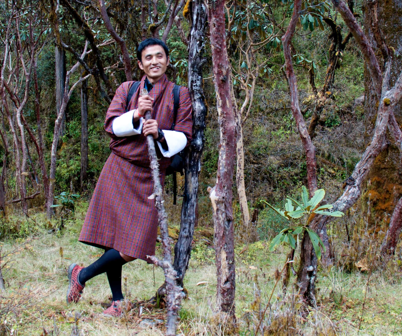 Man in Bhutanese clothing leaning against tree