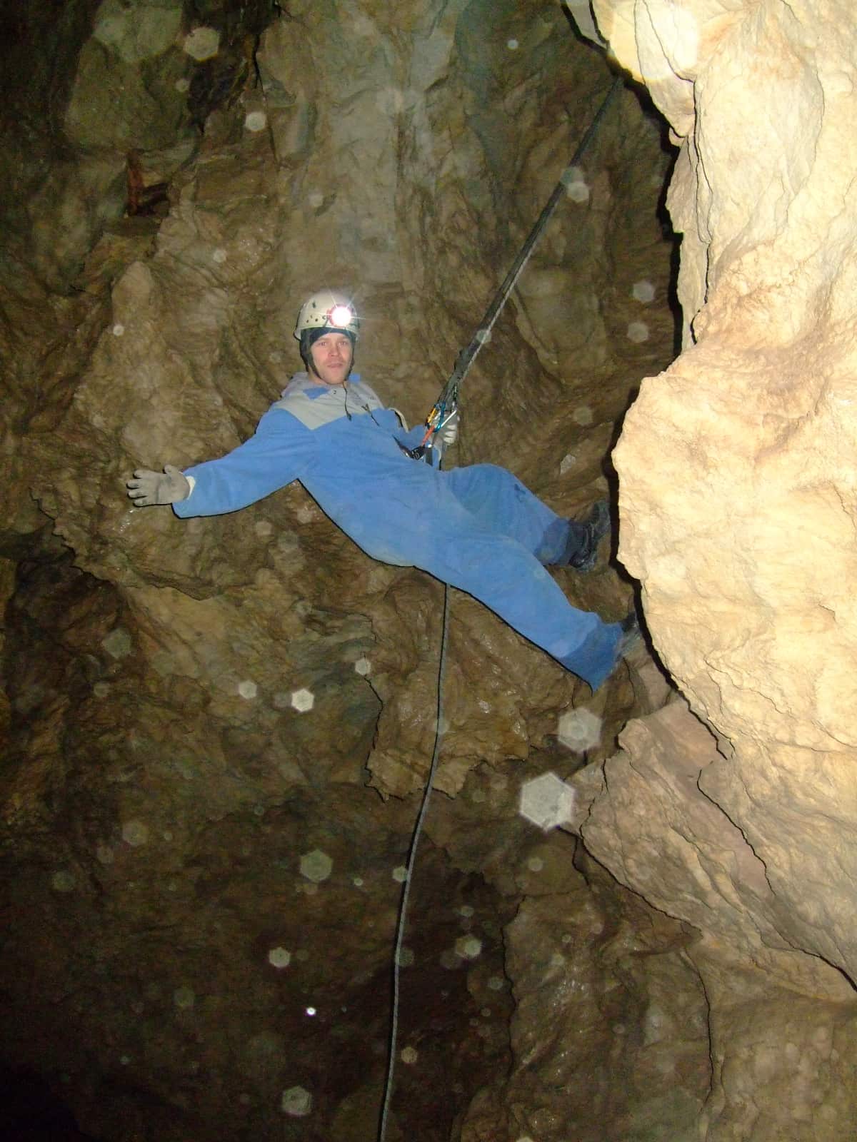 Man in blue coveralls abseling down rock face in cave
