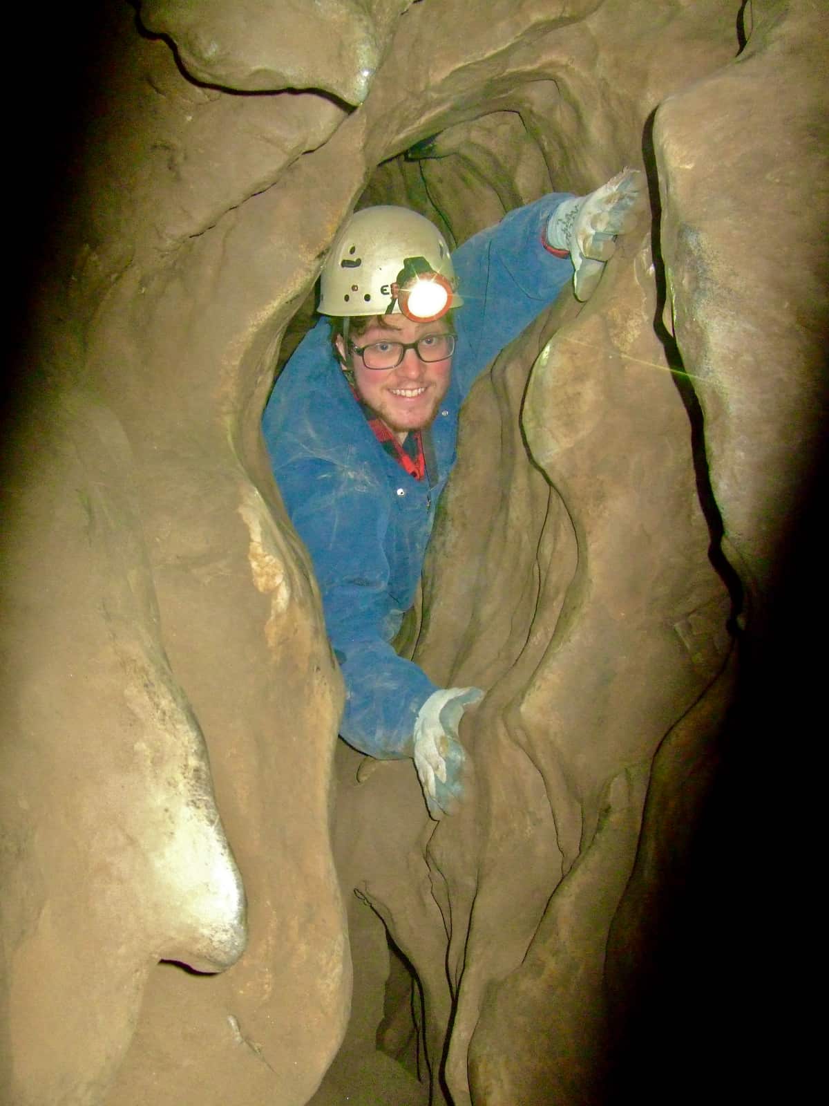 Man in blue coveralls squeezing through narrow cave