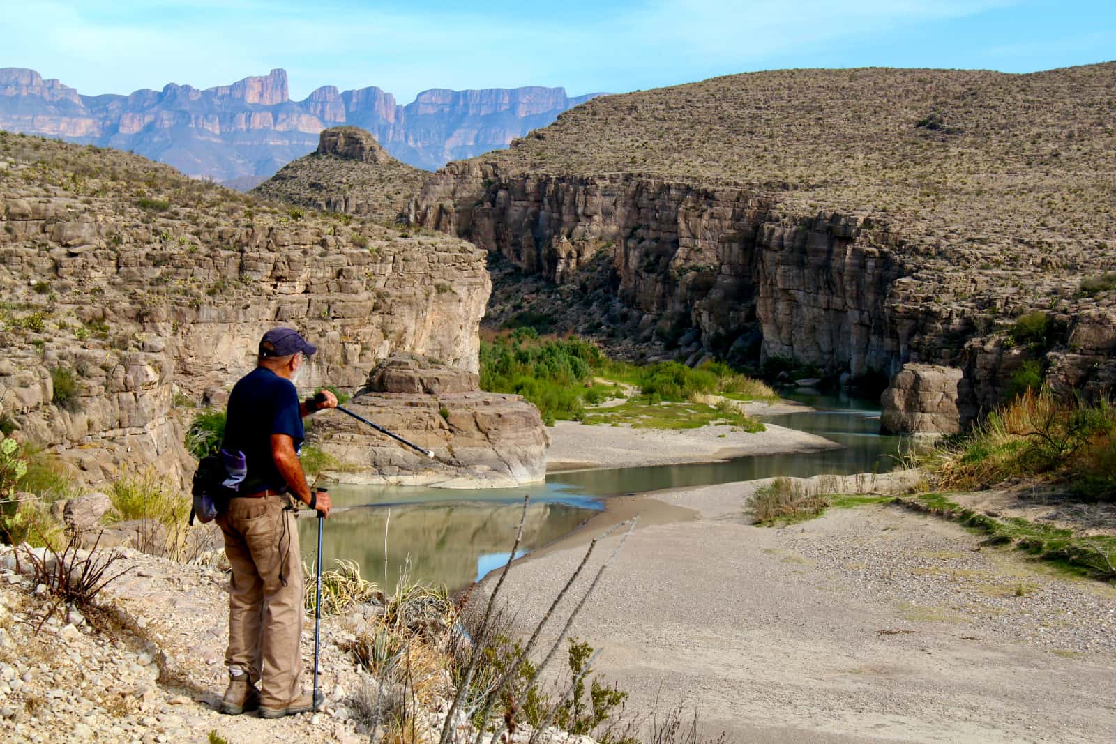 Man in blue shirt pointing pole toward river in canyon