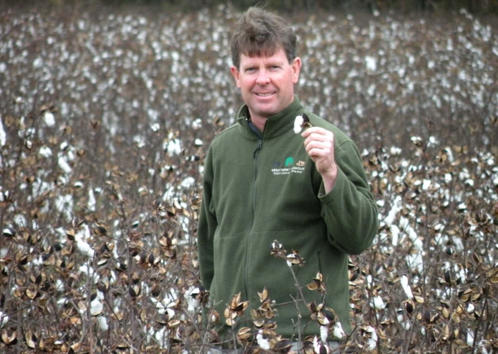Man in green sweater standing in field with fuzzy flowers