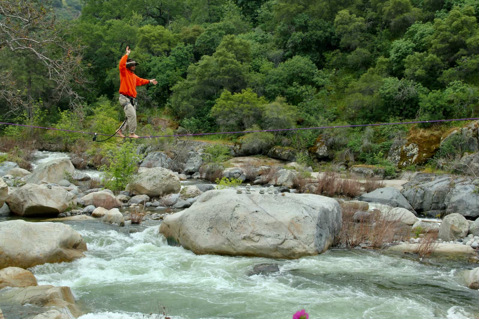 Man in orange sweater walking along rope over river
