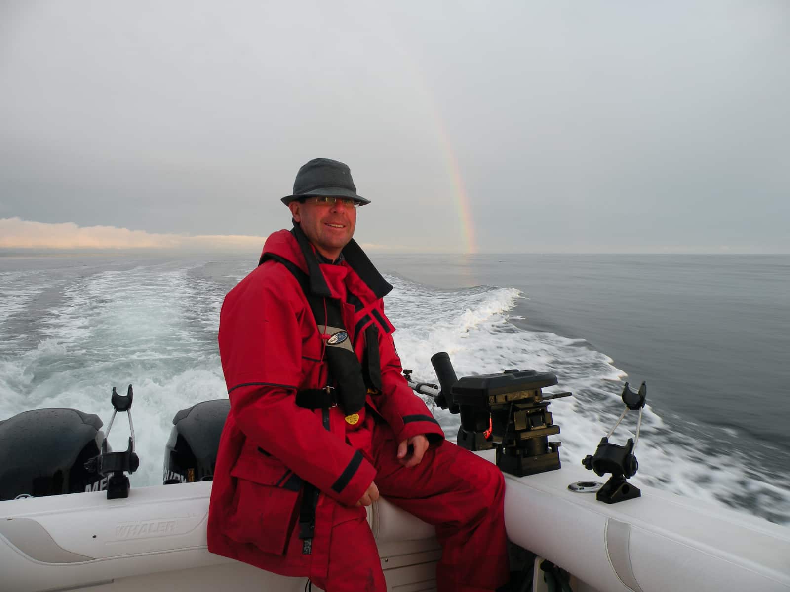 Man in red jacket sitting on boat with rainbow in background