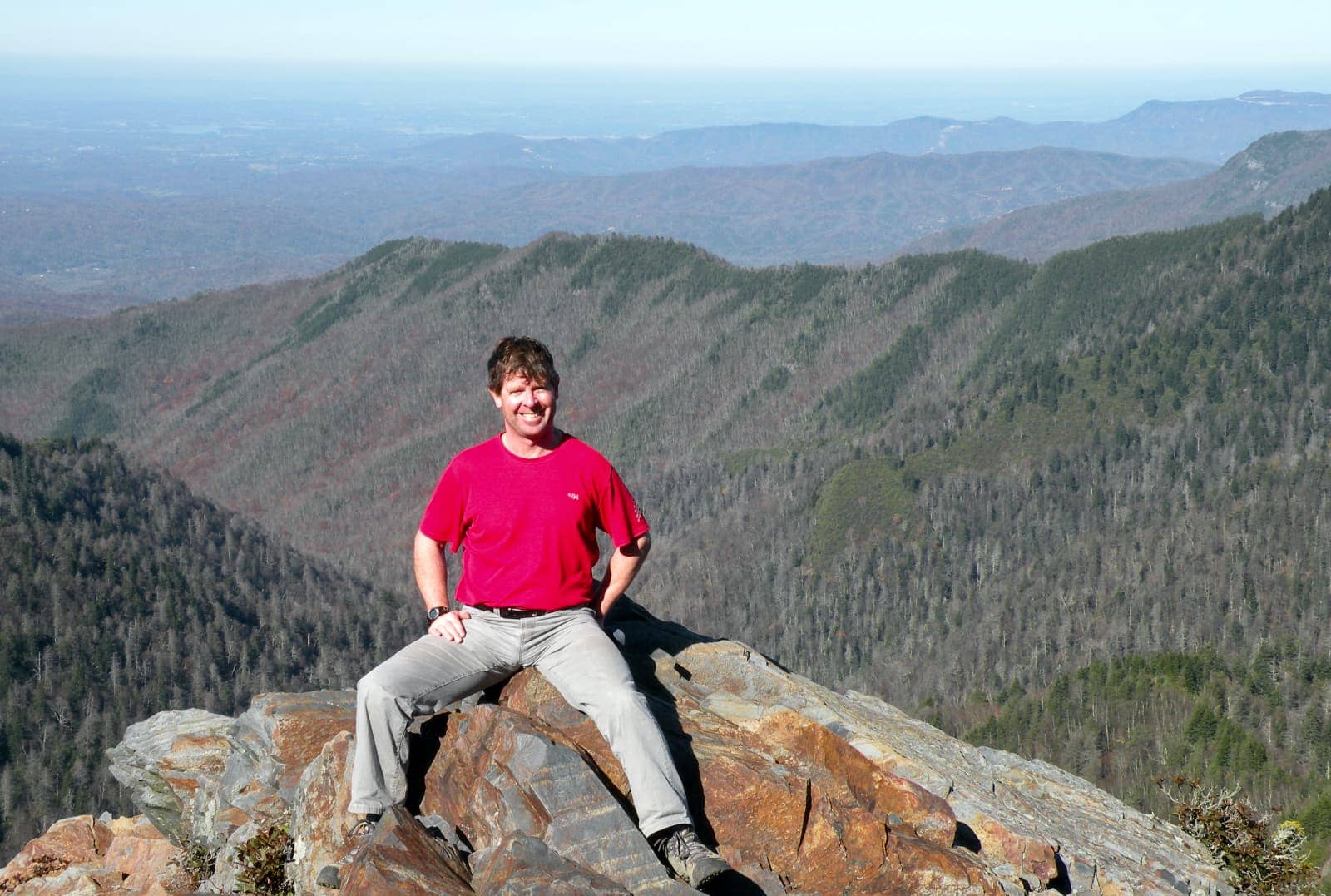 Man in red shirt smiling while sitting on rock