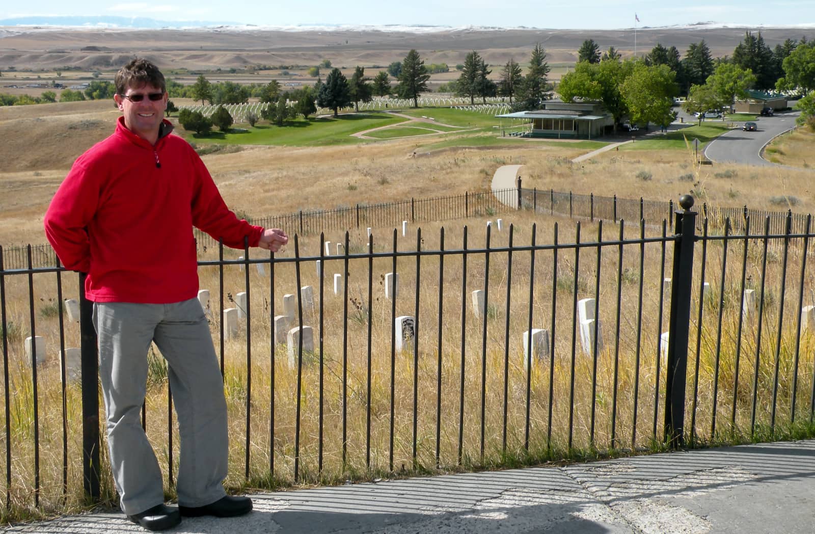 Man in red sweater standing against fence surrounding graves