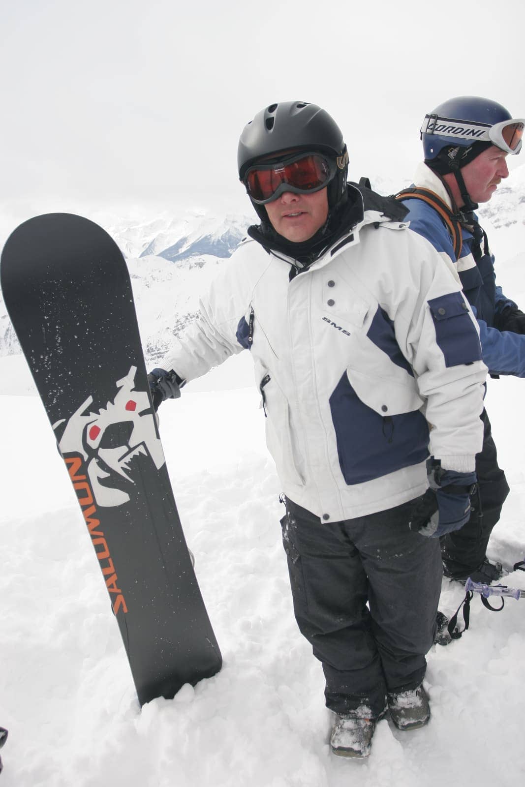 Man in white and blue jacket standing with snowboard