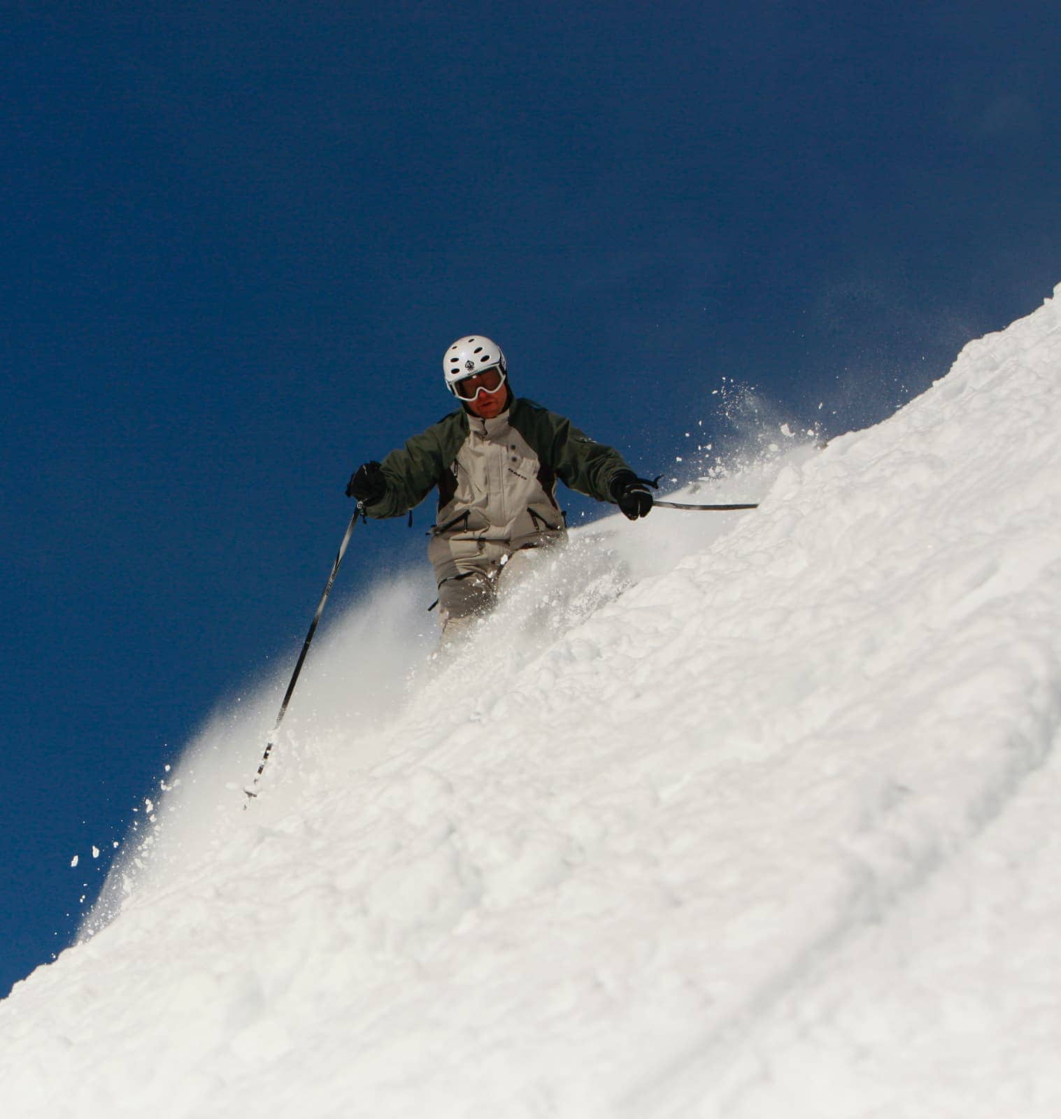 Man in white and green jacket skiing down hill