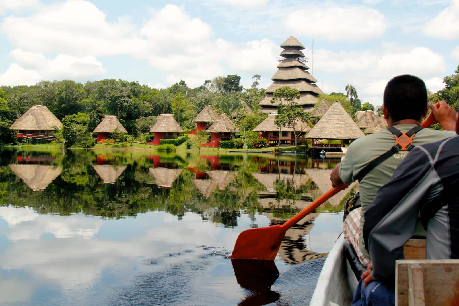 Man paddling canoe towards riverside village