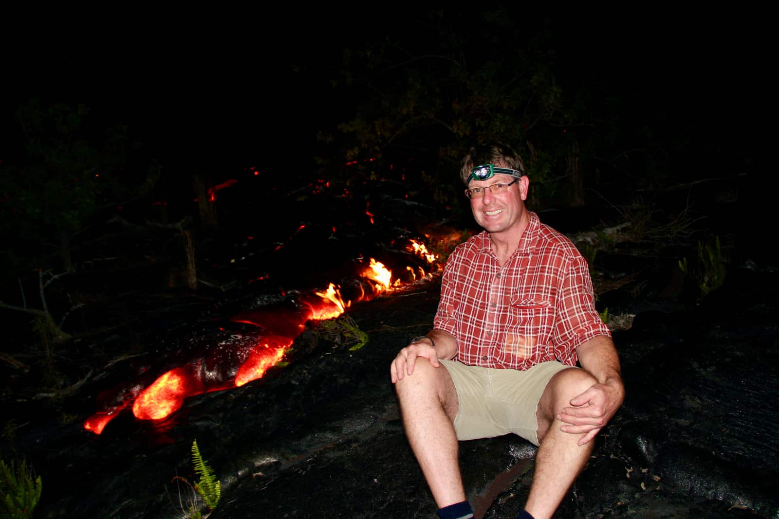 Man smiling in foreground with flowing lava in background