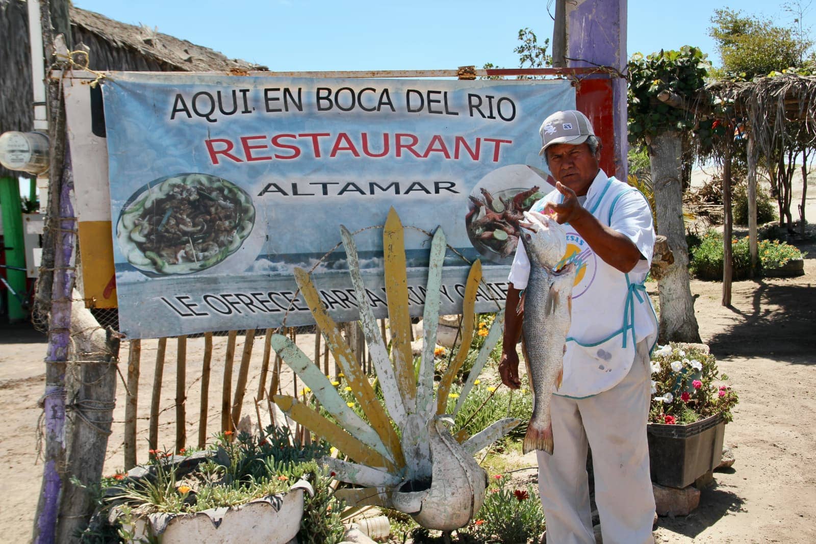 Man standing with freshly caught fish in front of restaurant sign