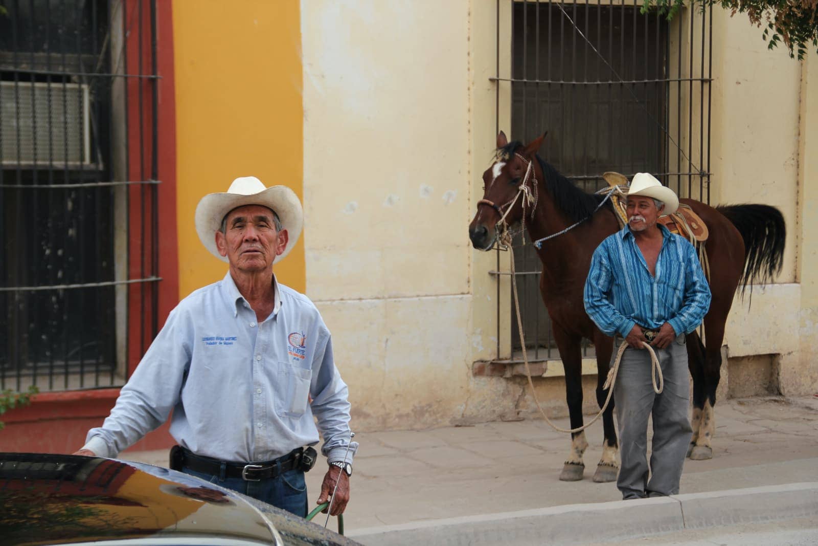 Man with blue shirt and jeans in foreground and man with horse in background