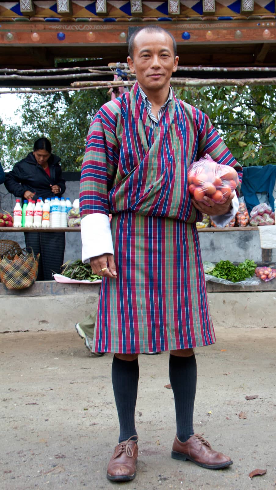 Man with colourful striped robe standing with bag of produce in hand