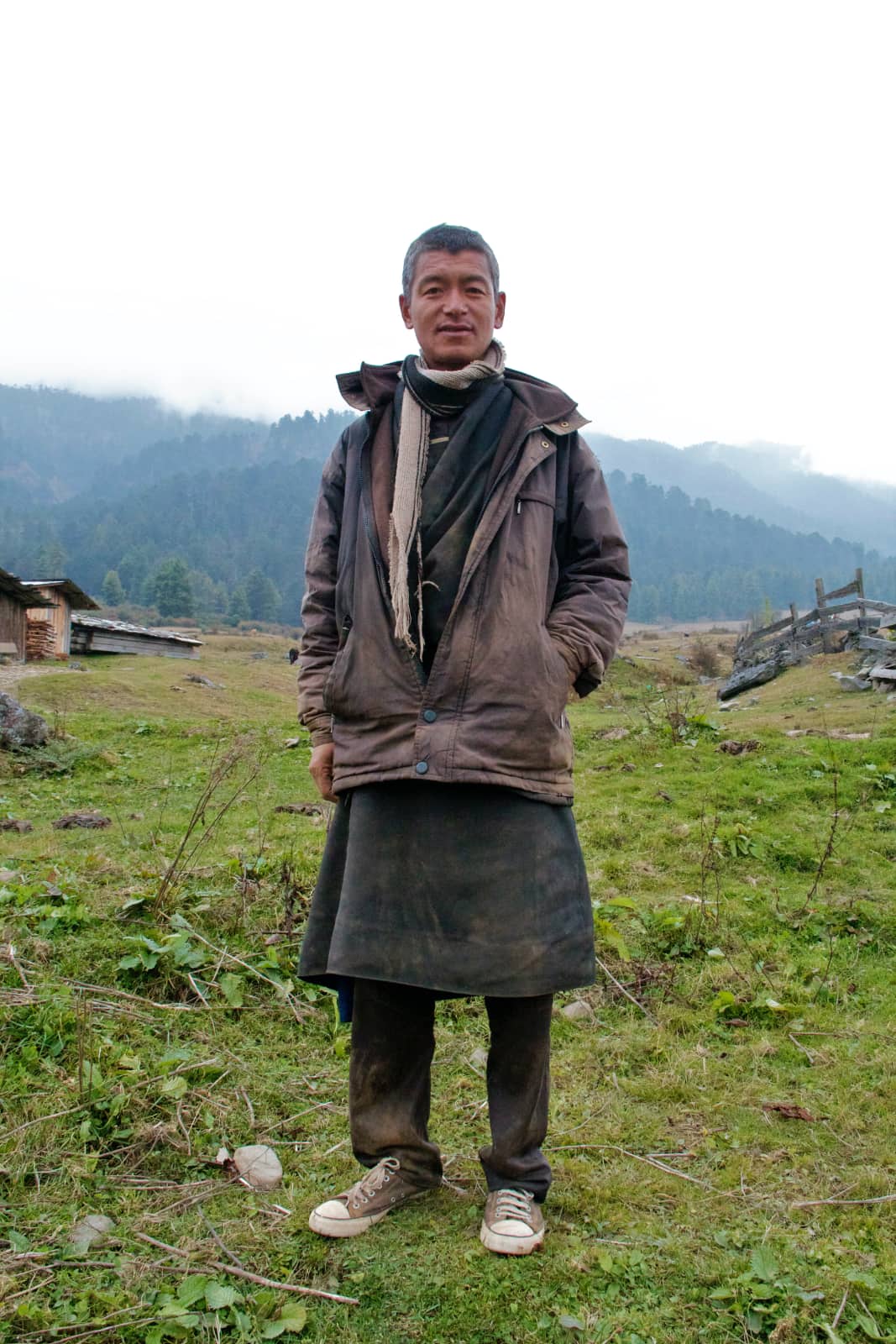 Man with dark clothing standing on grass with mountains in background