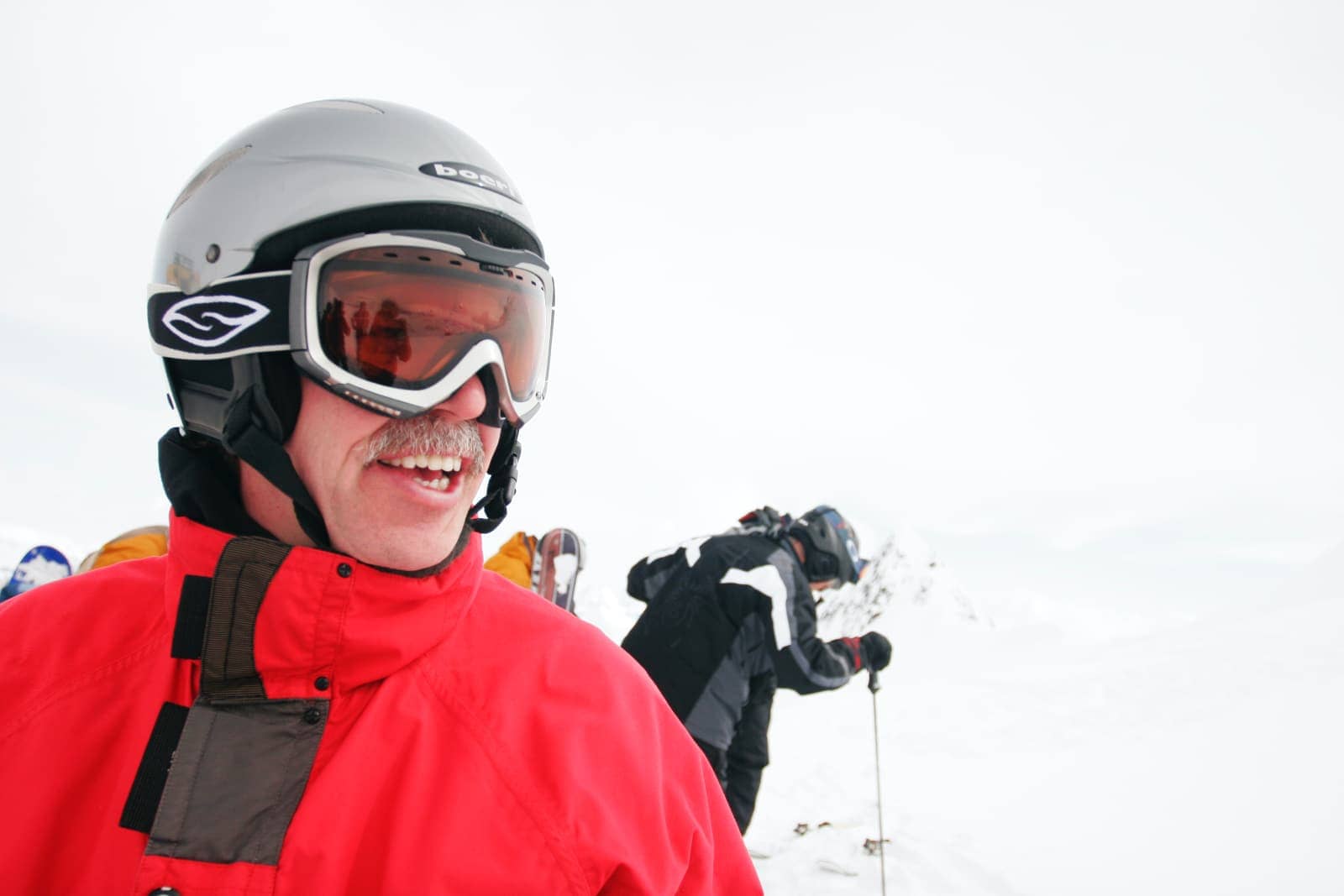 Man with orange tinted goggles and red jacket skiing