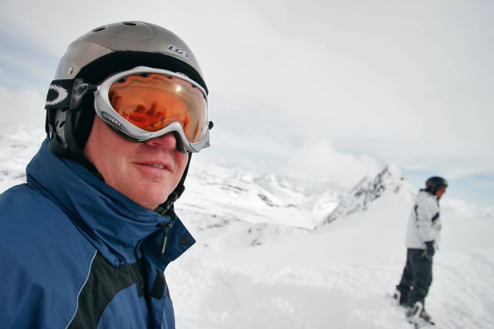 Man with orange tinted ski goggles and blue jacket