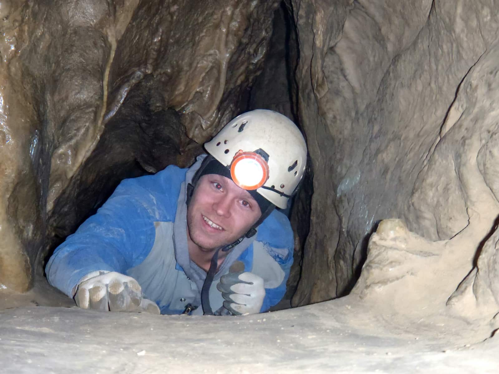 Man with white helmet crawling through cave