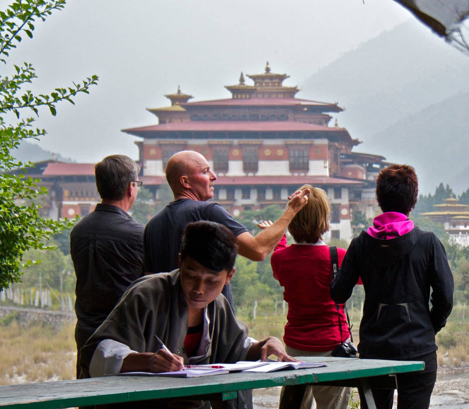 Man writing in notebook in foreground with four people admiring temple in background