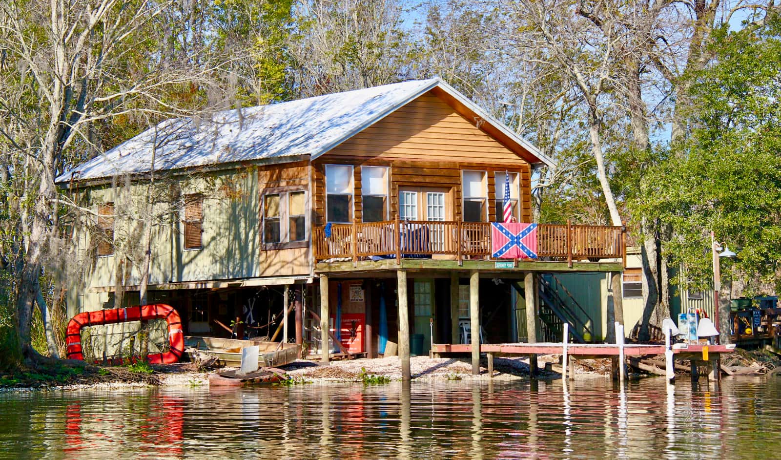 Old cabin sitting on shore of river with Confederate flag