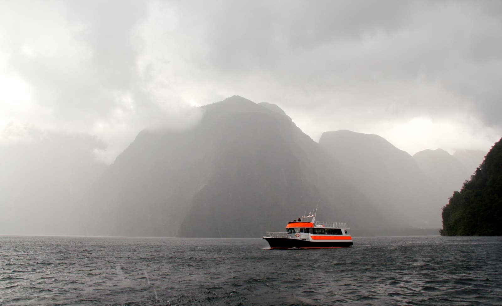 Orange and white boat sailing in fjord