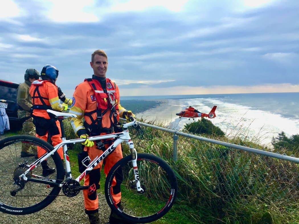 Search and rescue crew member holding mountain bike with helicopter in background