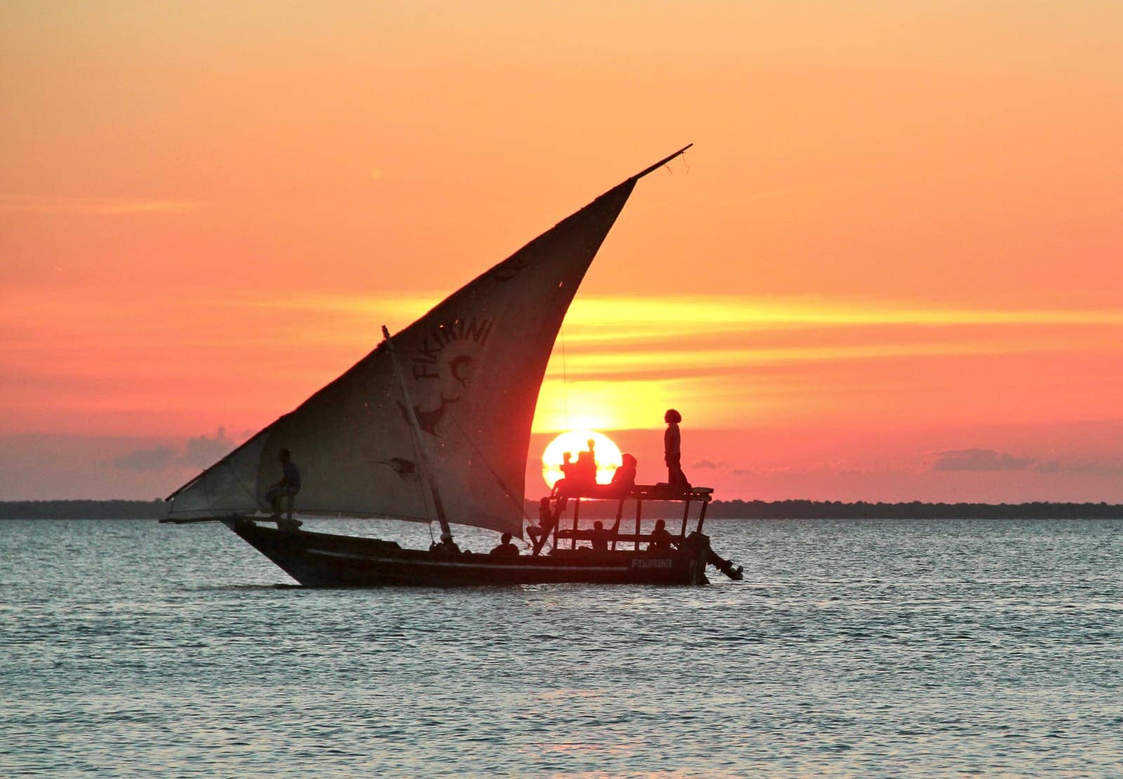 Small sail boat with multiple people on board sailing at sunset