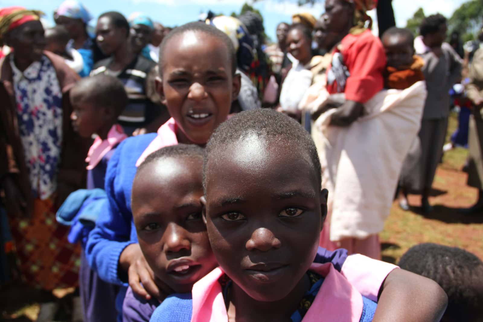 Three African children in foreground with groups of African people in background