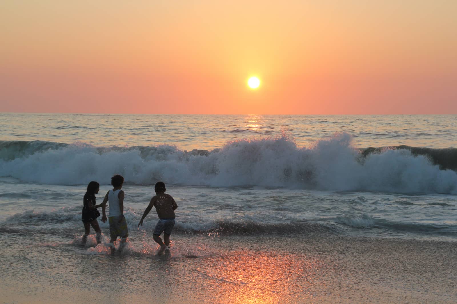 Three young children playing in ocean at sunset