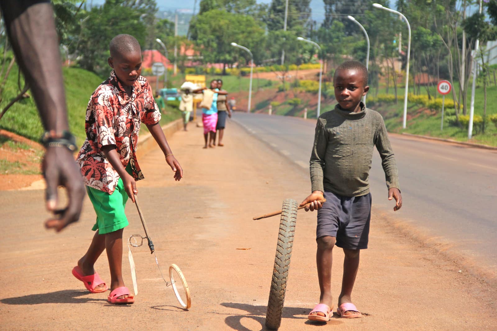 Two African children playing with sticks and wheels on roadside