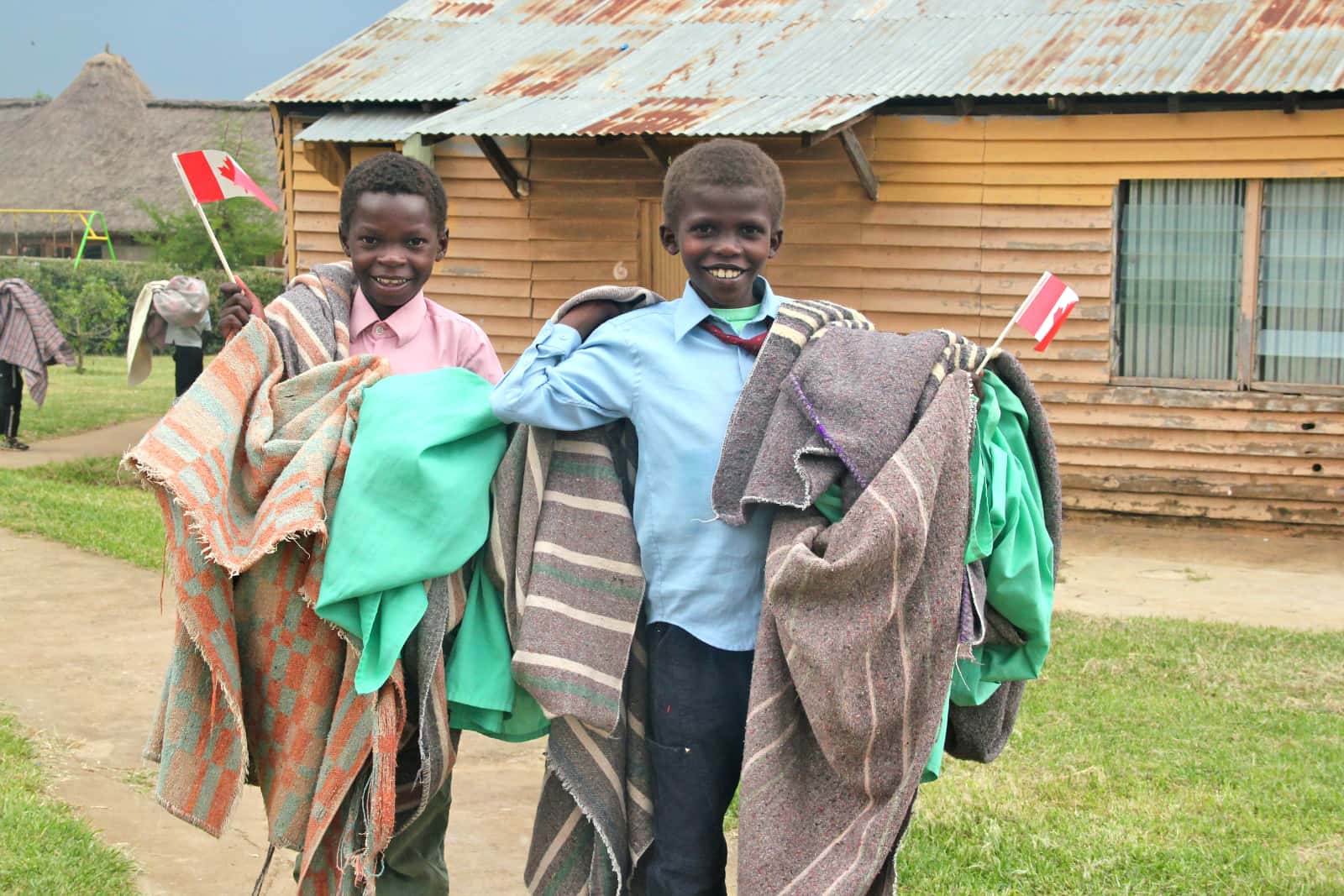 Two African children smiling with blankets and Canadian flags in hands