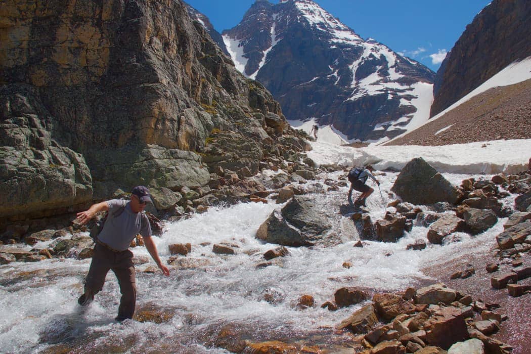 Two hikers crossing fast moving glacier water