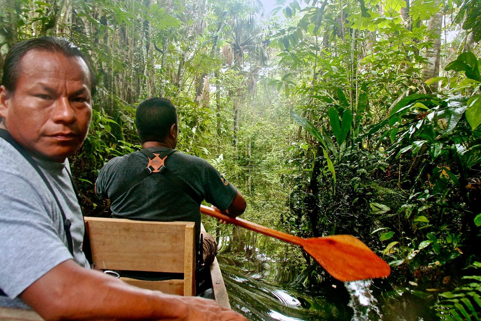 Two indigenous men paddling canoe along treed river